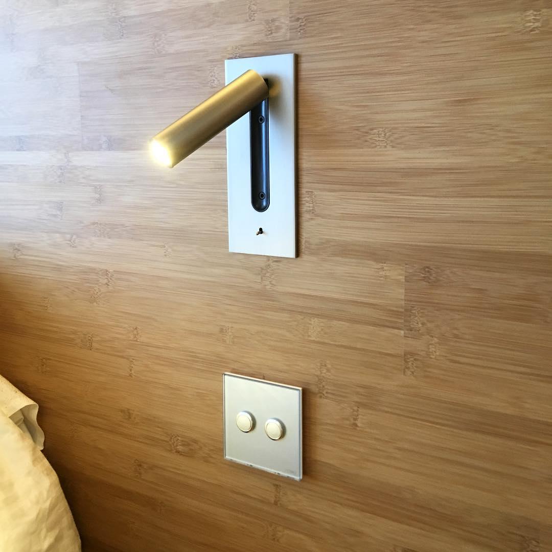 Fixed to a wood-panelled wall above a light switch, this Clérachic reading light in copper glows at an angle.