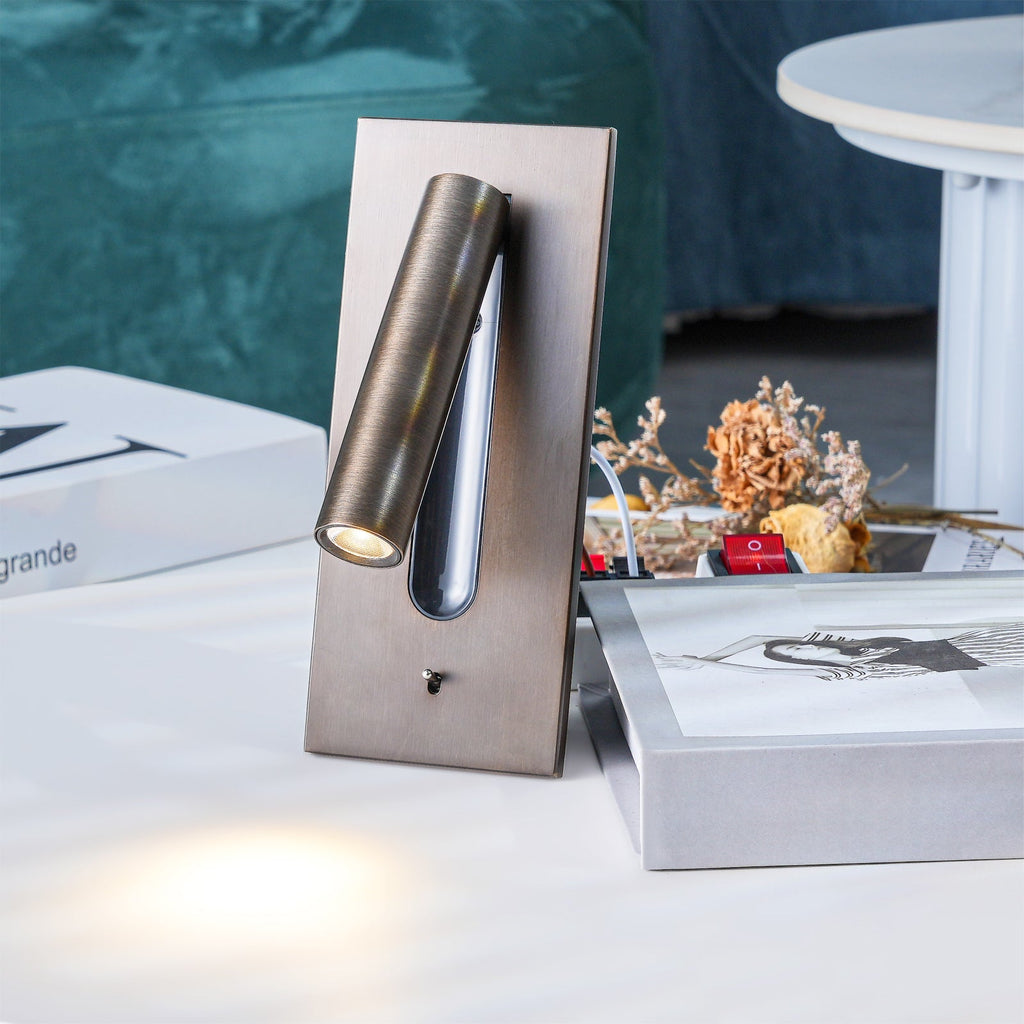 This Clérachic reading light in bronze rests on a table beside a box and dried flowers, its beam angled down onto papers.