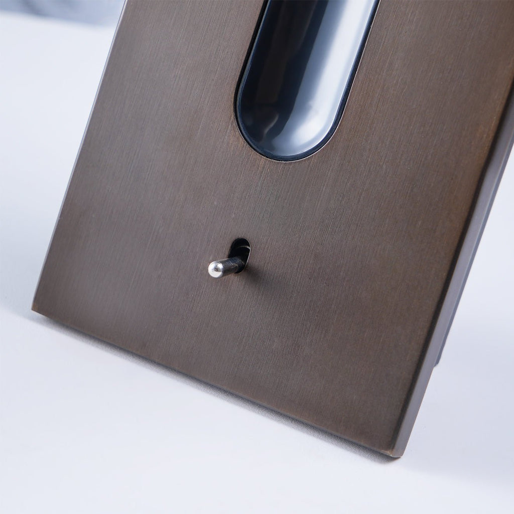 Close view of the bronze wall plate and small push switch on this Clérachic reading light, unlit.