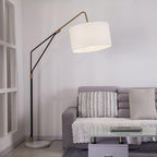 Clérachic black arc floor lamp arched over a grey tufted sofa with striped cushions, beside a glass-top coffee table.