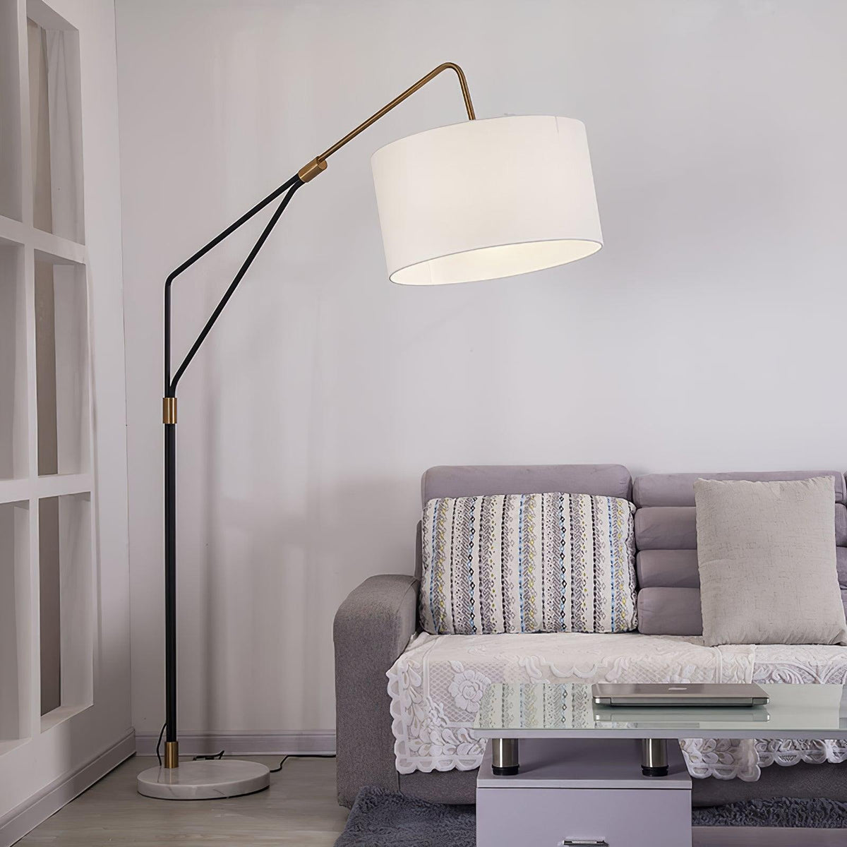 Clérachic black arc floor lamp arched over a grey tufted sofa with striped cushions, beside a glass-top coffee table.