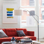 A brick-walled loft holds the Clérachic black arc floor lamp, arched over a red sofa with books and a small vase on the table.