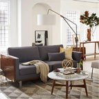 Clérachic black arc floor lamp arched over a grey sectional sofa with a mustard cushion, near an arched window and rug.