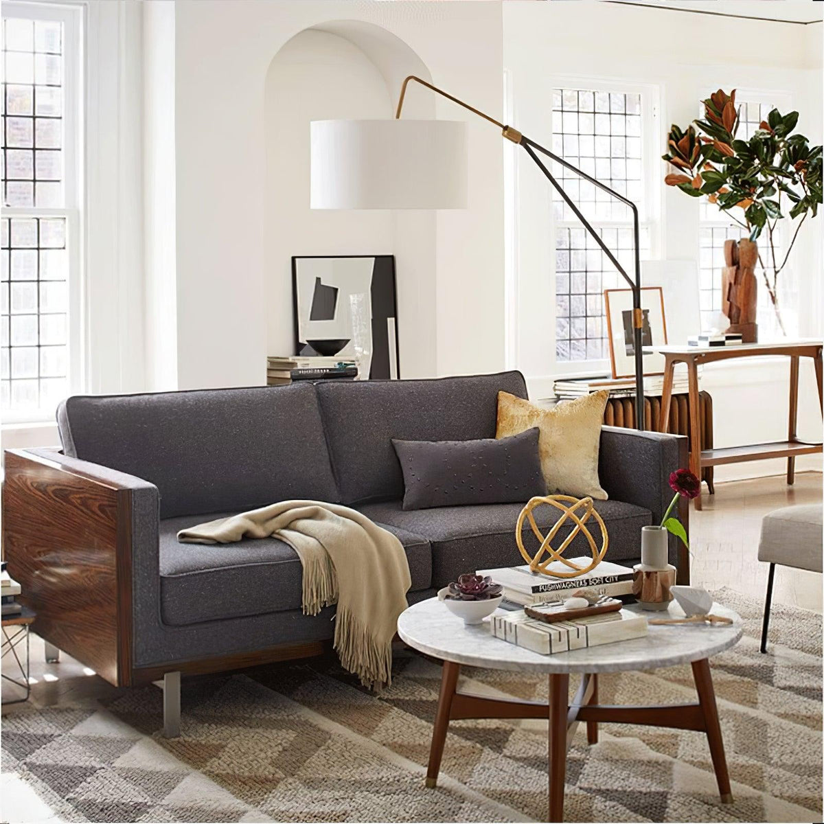 Clérachic black arc floor lamp arched over a grey sectional sofa with a mustard cushion, near an arched window and rug.