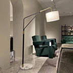 A vaulted interior frames the Clérachic black arc floor lamp, positioned beside dark green velvet chairs and open shelving.