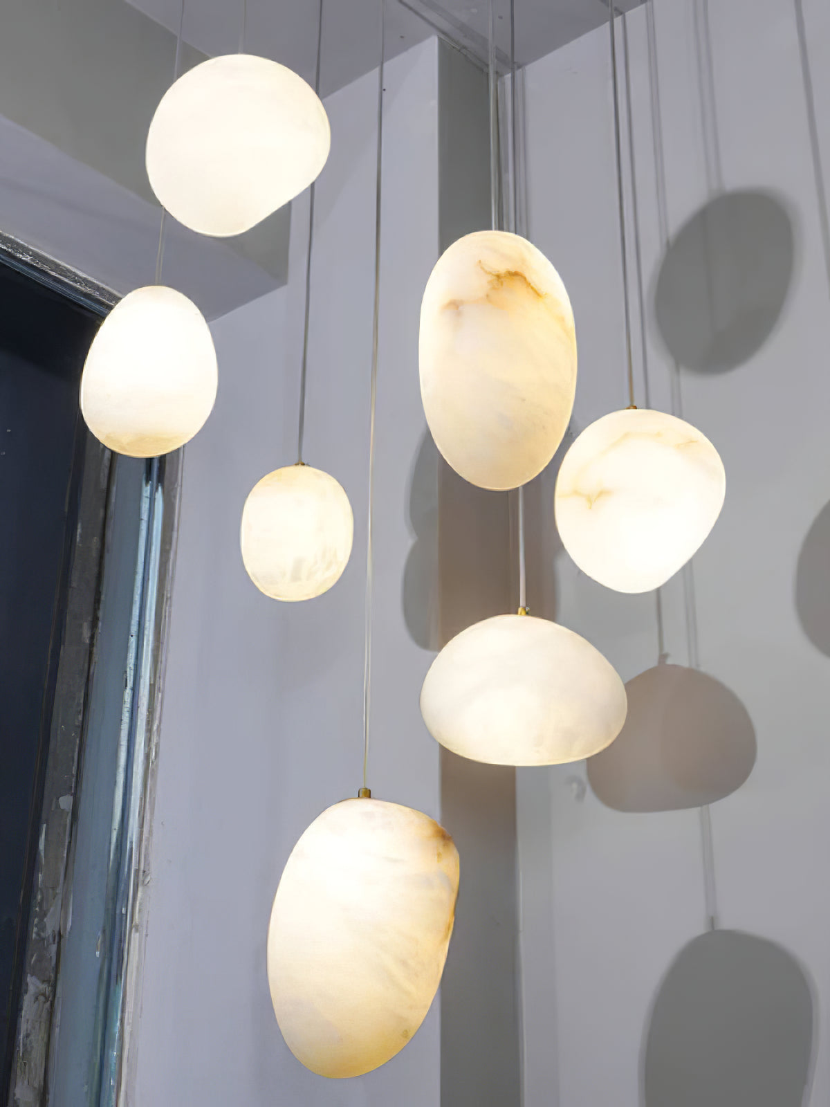Seven alabaster shades clustered at varied heights, lit and casting soft shadows on the wall