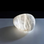 A single alabaster stone lit from within, resting on a pale surface against black