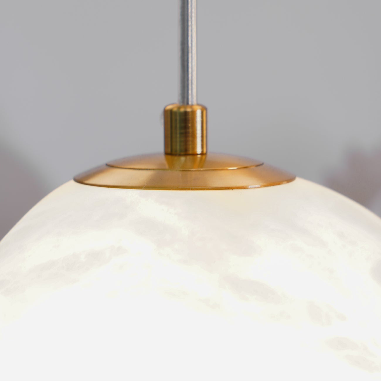 Close-up of the brushed brass canopy cap where the cable meets the alabaster shade