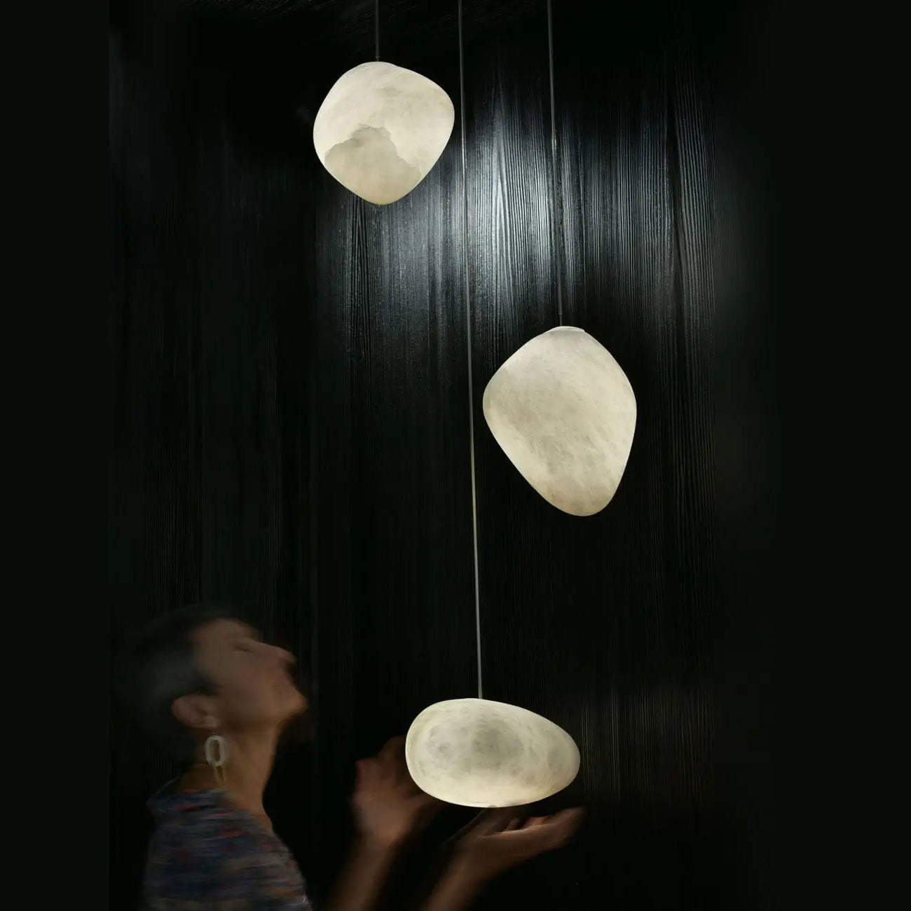 Three lit alabaster shades in a dark room with a person reaching up to the lowest one