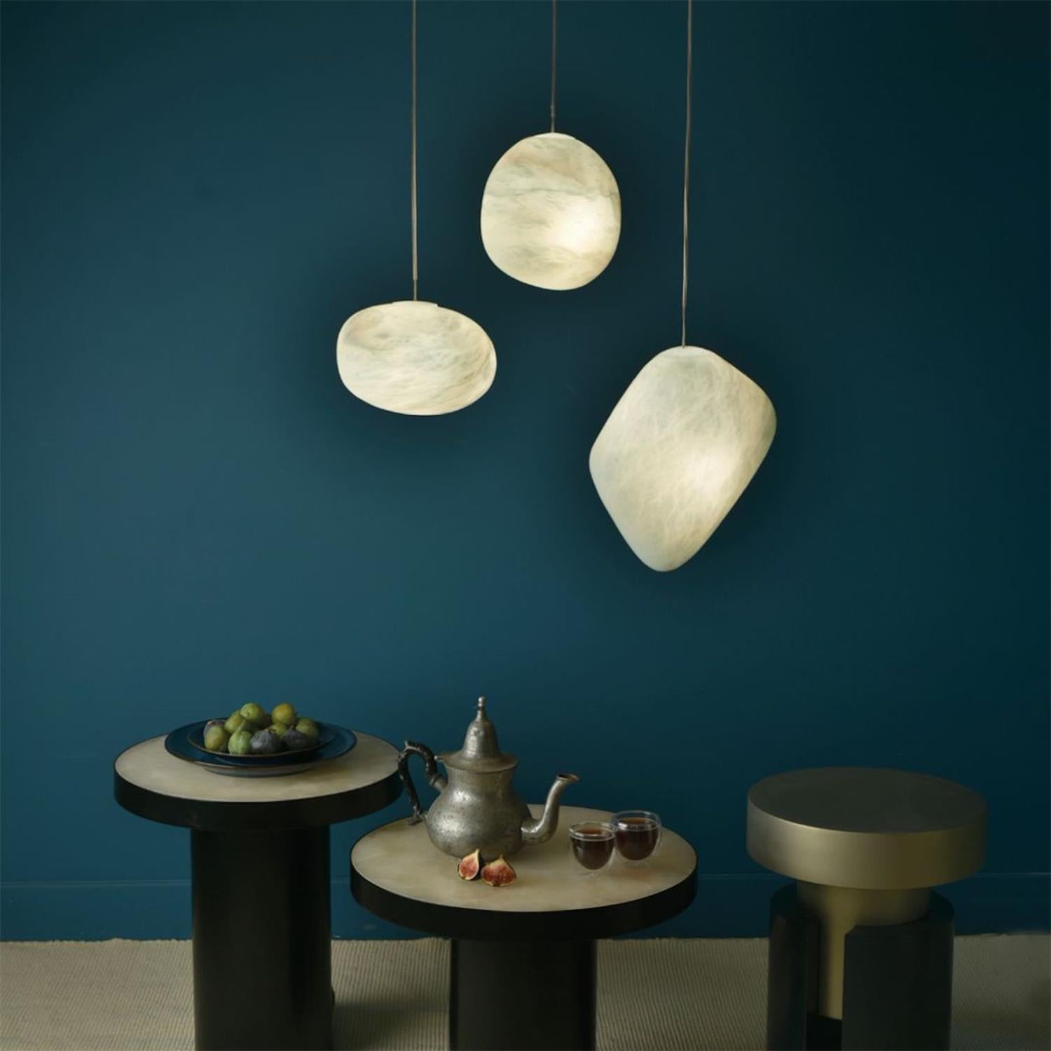 Three alabaster shades glowing above small round tables against a deep teal wall
