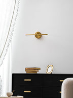 Low-angle view of this gold-finish Clérachic wall light, unlit, above a black dresser with books, a frame, and a small bowl.