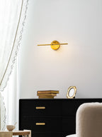 At a low angle, this gold-finish Clérachic wall light glows warmly above a black dresser beside a cream armchair.