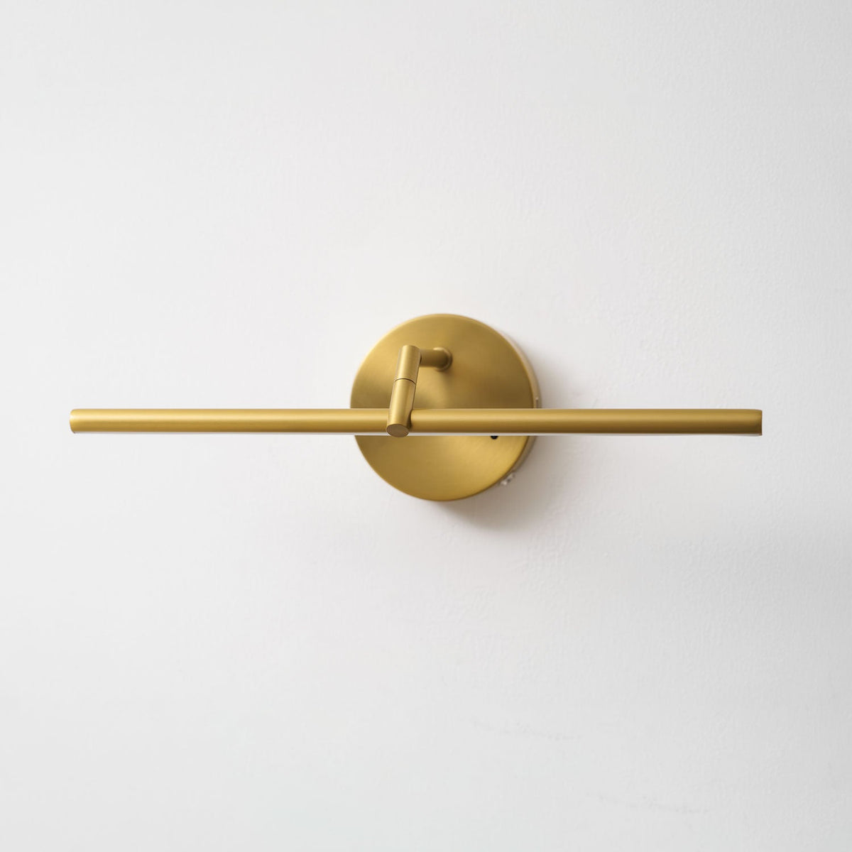 This gold-finish Clérachic wall light shown unlit on a plain wall, the bar centred through the canopy with the pivot arm visible above.