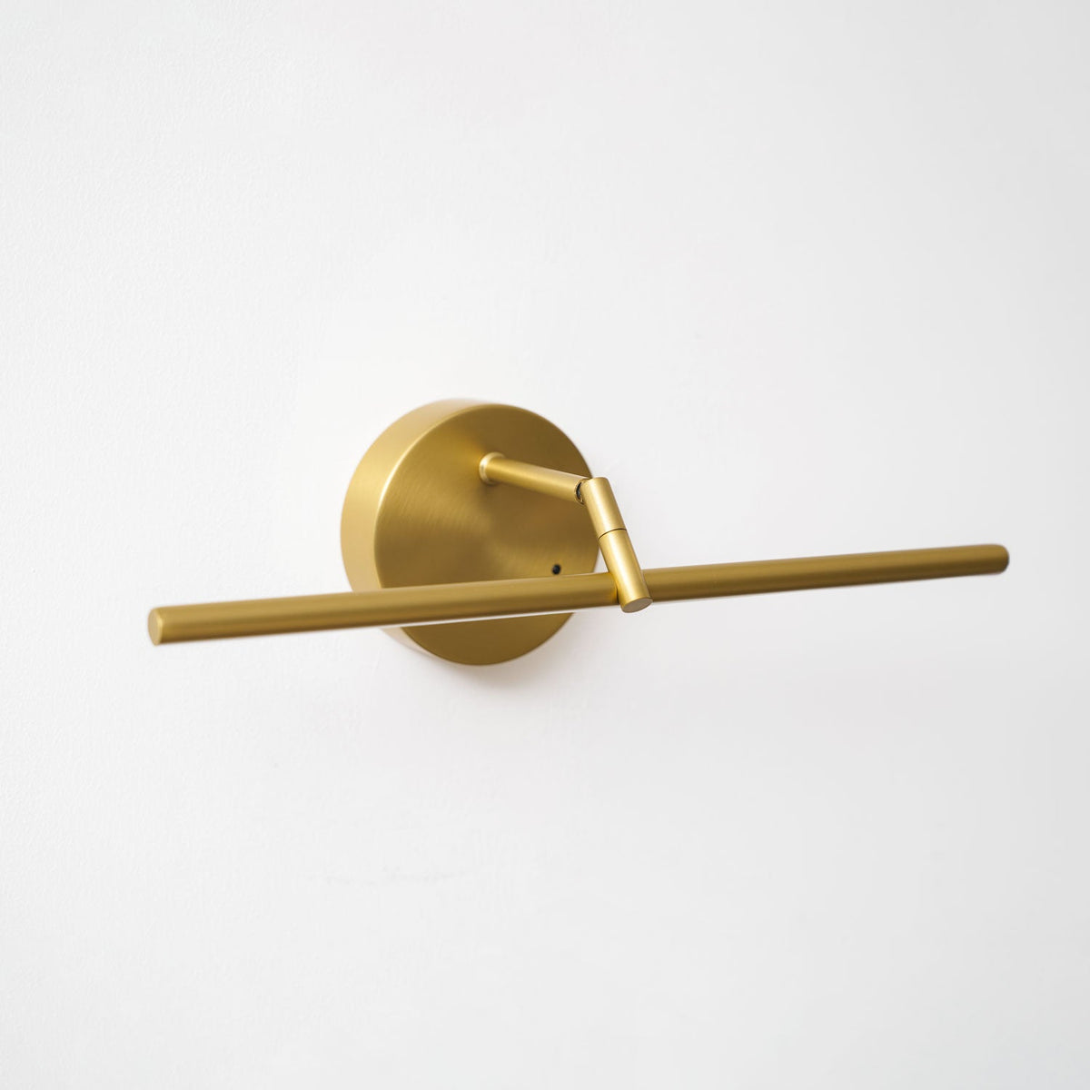 This gold-finish Clérachic wall light shown unlit at an angle, the canopy to one side and the bar extending diagonally across the wall.