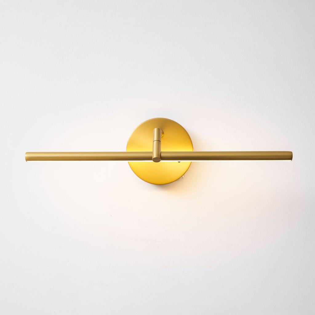 Straight-on, this gold-finish Clérachic wall light glows with the bar centred through its round canopy.