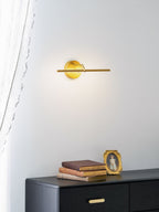 Unlit gold-finish wall light from Clérachic mounted above a black dresser with stacked books and a small framed portrait.