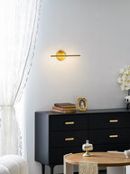 This gold-finish Clérachic wall light glows above a black dresser and a round table set with a cloche and an orchid, curtain beside it.