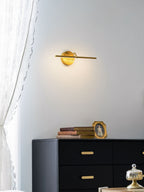 Mounted above a black dresser with brass drawer pulls, this gold-finish Clérachic wall light glows beside stacked books and a framed portrait.