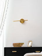 Low-angle view of this gold-finish Clérachic wall light, unlit, above a black dresser with books and an oval gilt frame.