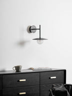 White Clérachic wall light shown unlit above a black dresser with brass drawer pulls.