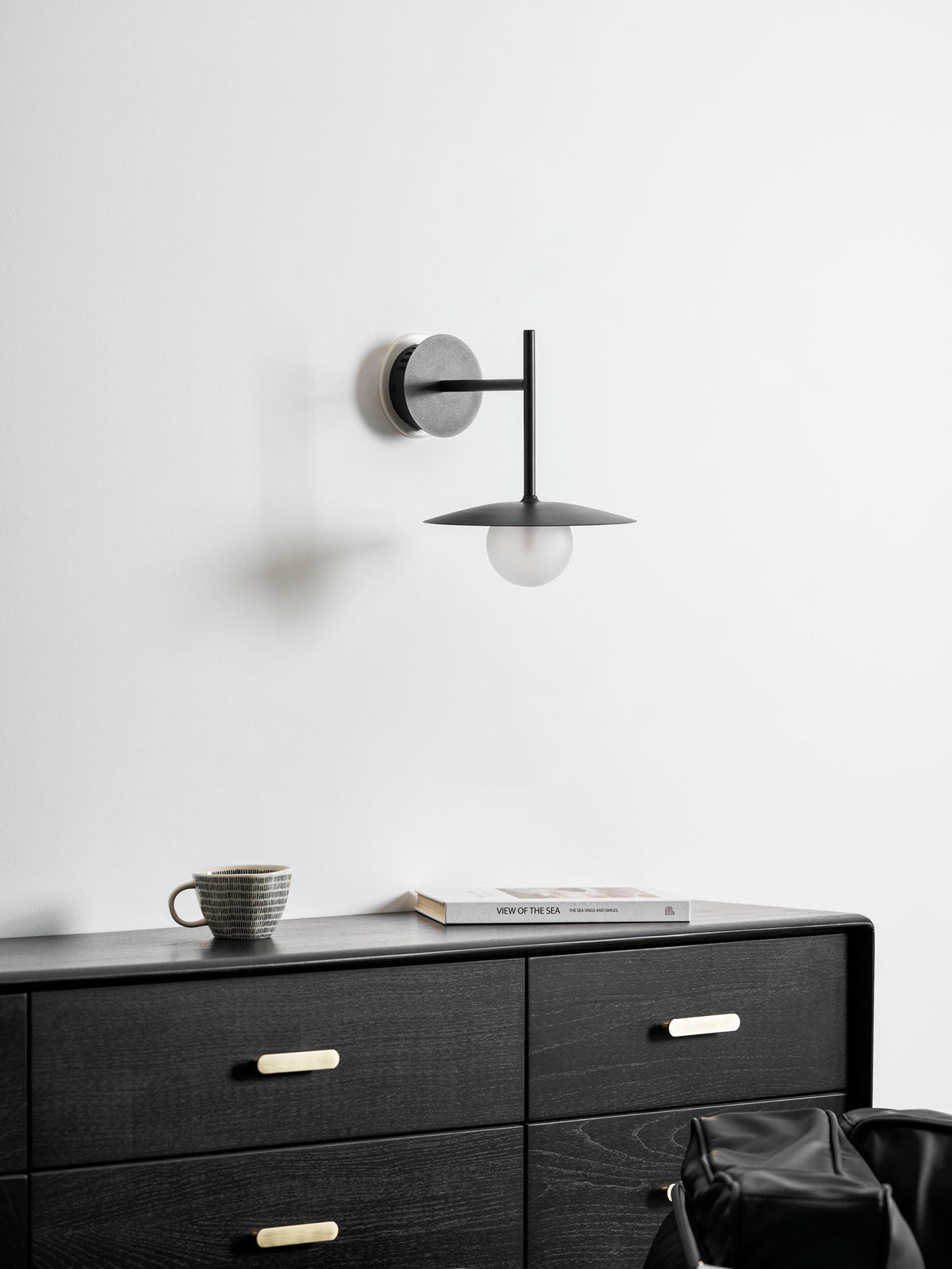 White Clérachic wall light shown unlit above a black dresser with brass drawer pulls.