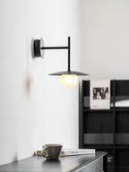 Grey Clérachic wall light glows above a dresser holding a cup and a stacked book.