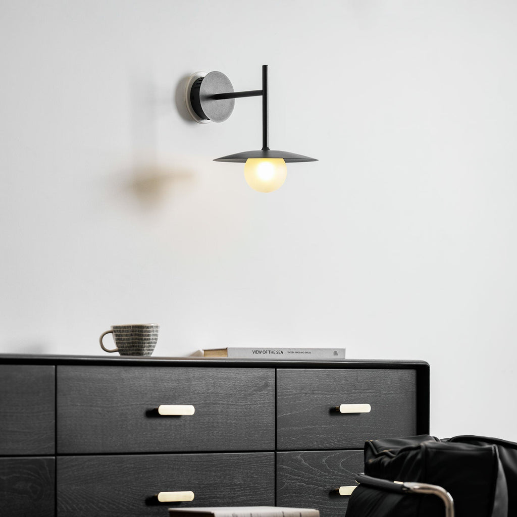 Grey Clérachic wall light glows above a dresser set with a mug and folded books.