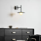 Grey Clérachic wall light glows above a dresser set with a mug and folded books.