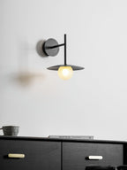 Grey Clérachic wall light glows above a dresser with a small cup and a stack of books.