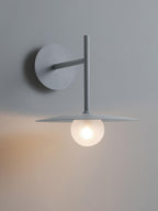 Grey Clérachic wall light shown unlit, its full angled arm and disc shade against a plain wall.