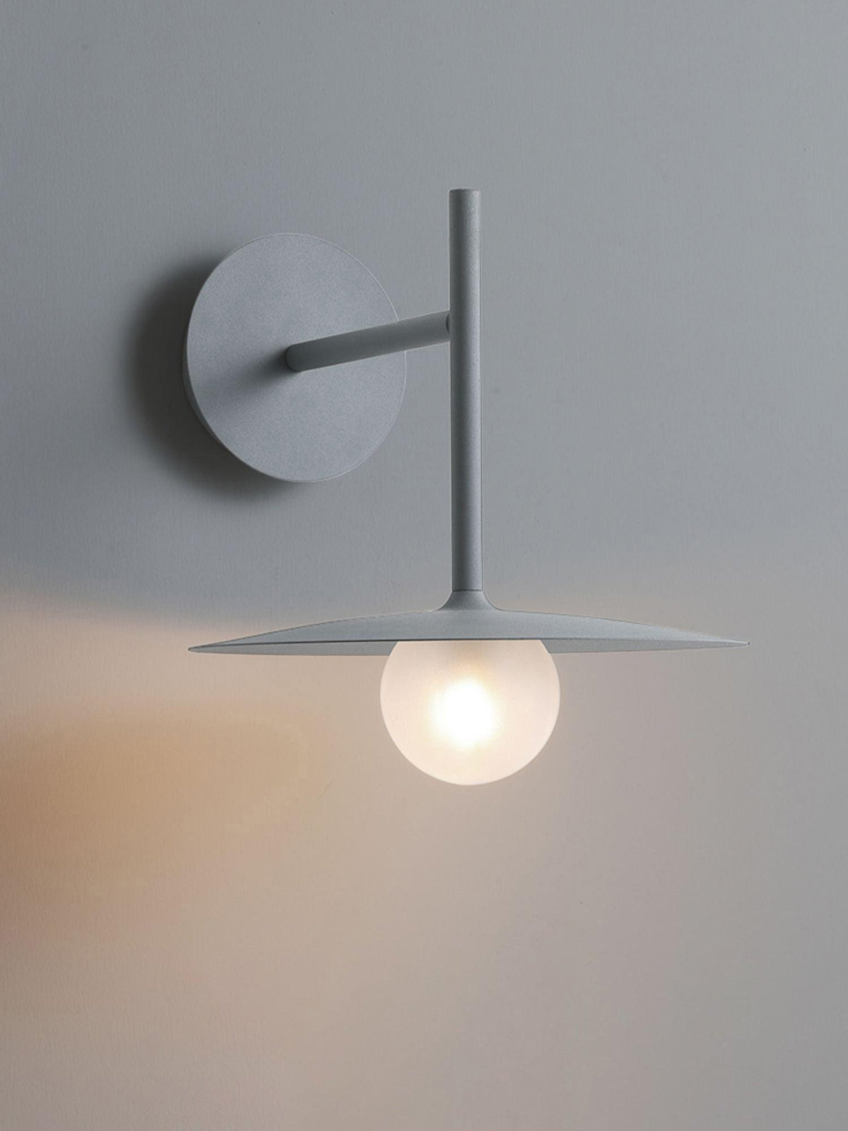 Grey Clérachic wall light shown unlit, its full angled arm and disc shade against a plain wall.