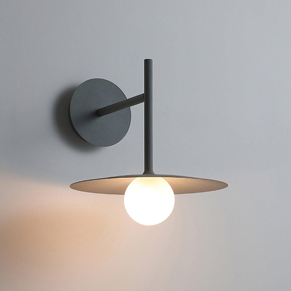 Studio side view of this black Clérachic wall light, its glass globe lit beneath the disc shade.