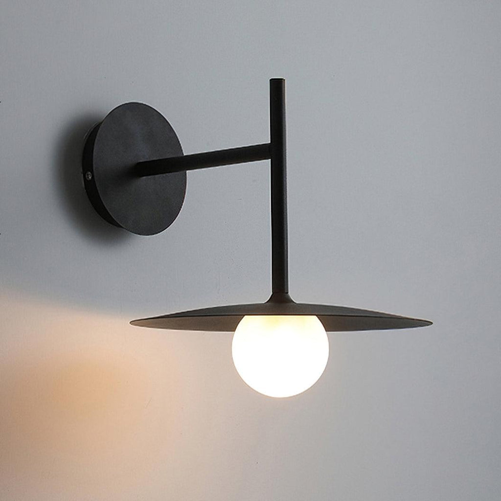 Side angle on the round wall plate and arm of this black Clérachic wall light, lit below.