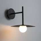 Side angle on the round wall plate and arm of this black Clérachic wall light, lit below.