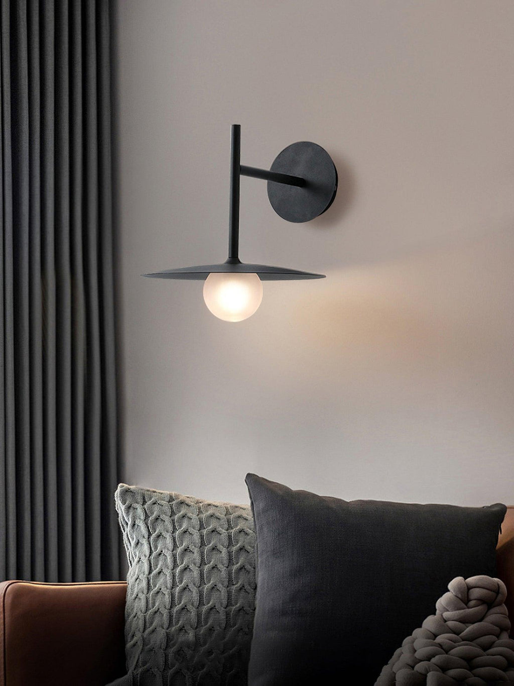 Beside charcoal cushions and heavy curtains, this black Clérachic wall light glows softly.