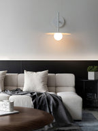 Grey Clérachic wall light lit above a pale sofa piled with a folded throw.