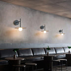 In a plastered café nook, three black Clérachic wall lights line the wall above a leather banquette.