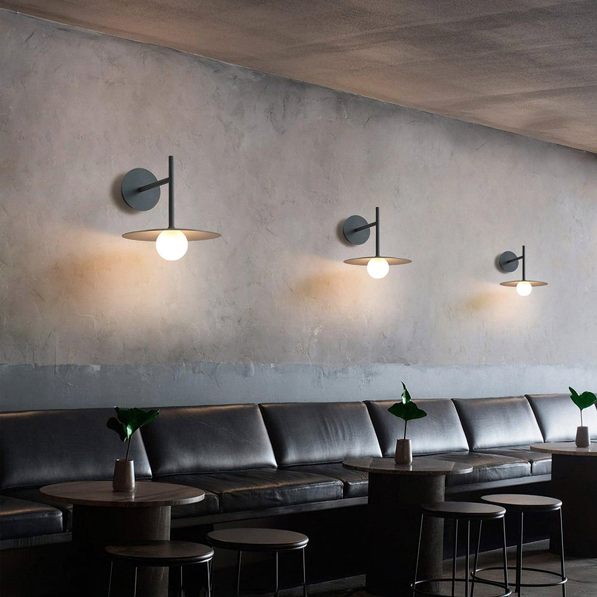 In a plastered café nook, three black Clérachic wall lights line the wall above a leather banquette.