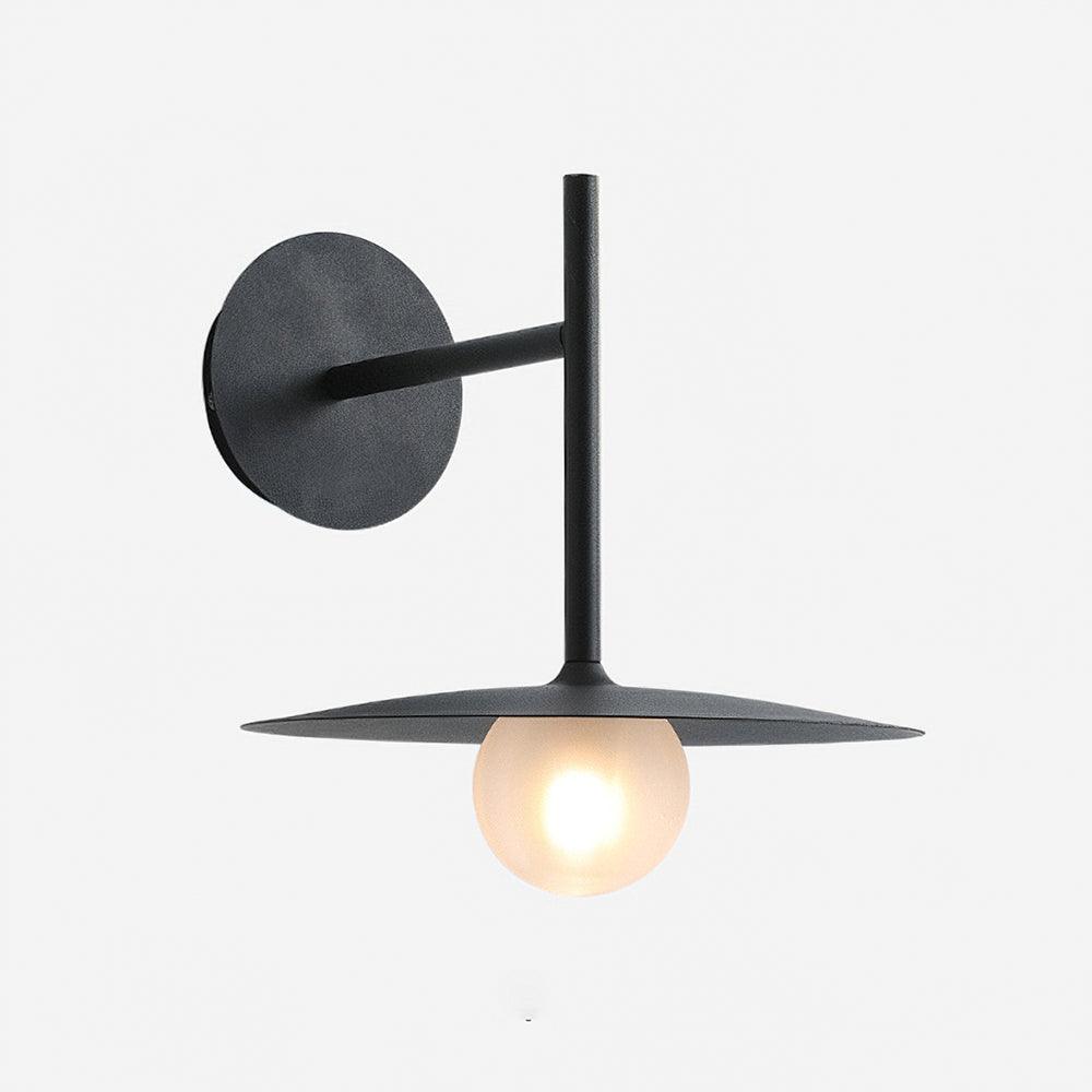 Studio view of this black Clérachic wall light, its disc shade glowing warmly.