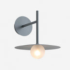 Studio view of this grey Clérachic wall light, its disc shade glowing warmly.