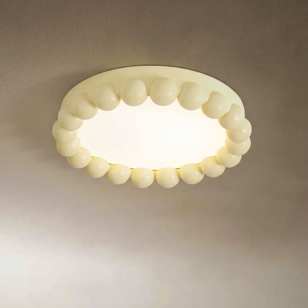 This Clérachic ceiling light in beige glows warmly, its beaded resin ring lit against a soft taupe backdrop.