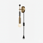 Clérachic plug-in wall lamp on white, dark stone beads above a lit glass globe and a black cord ending in a plug.