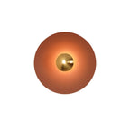 This orange Clérachic wall light glows warm on a plain background, its antique copper centre bright.