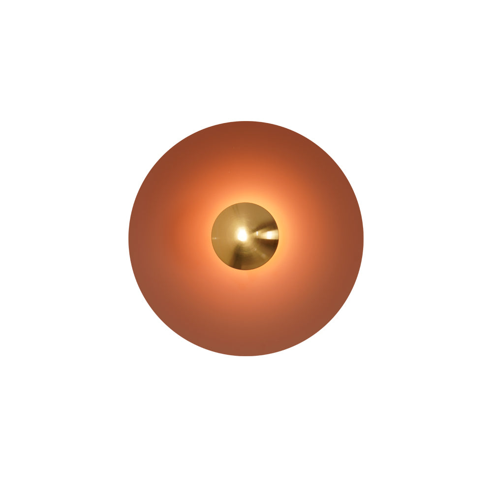 This orange Clérachic wall light glows warm on a plain background, its antique copper centre bright.