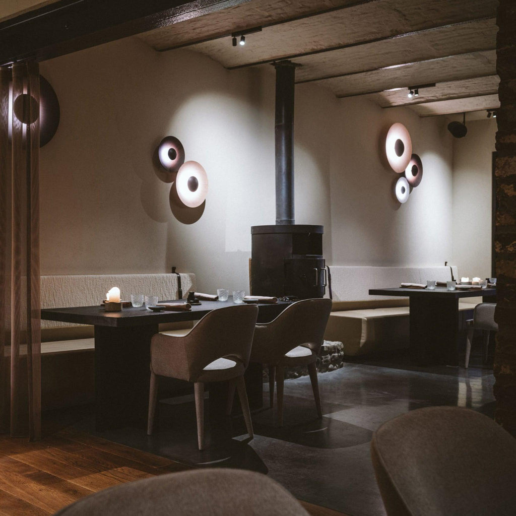 Grouped Clérachic wall lights glow warm in a rustic dining room with a wood-burning stove and beamed ceiling.