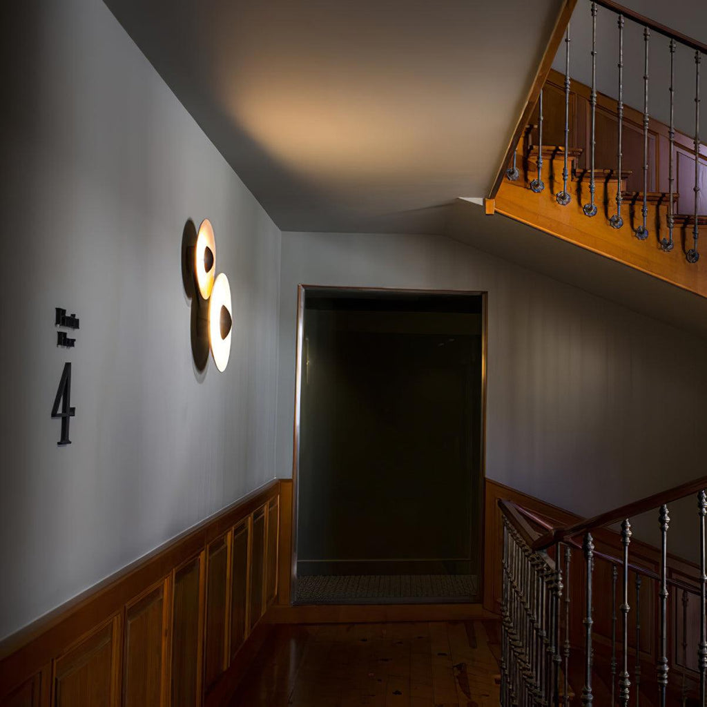 Two Clérachic wall lights, one glowing warm, mounted near a staircase landing marked with the number four.