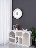 A white Clérachic wall light glows on a charcoal wall above a console table holding a framed photo and plant.