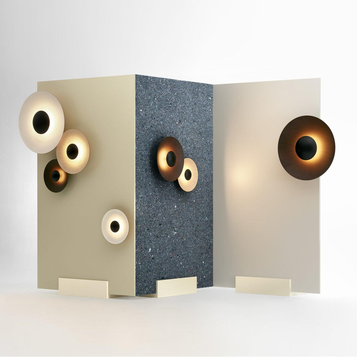 Several Clérachic wall lights of different sizes glow warm on a two-panel display, some lit and some dark.
