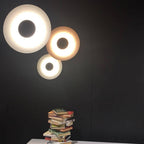 Three Clérachic wall lights glow warm on a black wall above a stack of books on a table.