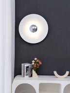 A white Clérachic wall light glows above a console table with books and flowers, against a charcoal wall.